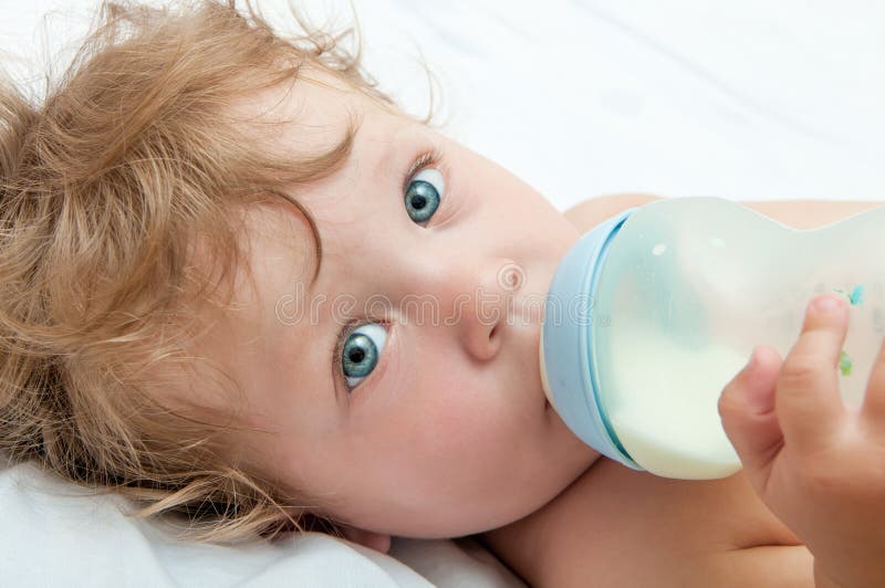 Kleines lockiges Baby saugt eine Flasche lizenzfreies stockbild Kleines lockiges Baby saugt eine Flasche lizenzfreies stockbild