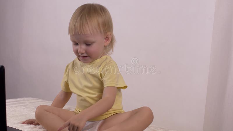 Kleines lächelndes blondes Mädchen bedrängt die Knöpfe auf dem Laptop und die Blicke in den Computer, Hintergrund stock video footage Kleines lächelndes blondes Mädchen bedrängt die Knöpfe auf dem Laptop und die Blicke in den Computer, Hintergrund stock video footage