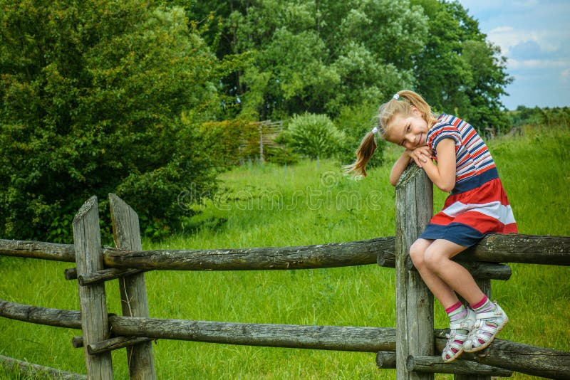 Kleines lächelndes Mädchen, das auf Bretterzaun sitzt lizenzfreie stockfotos Kleines lächelndes Mädchen, das auf Bretterzaun sitzt lizenzfreie stockfotos
