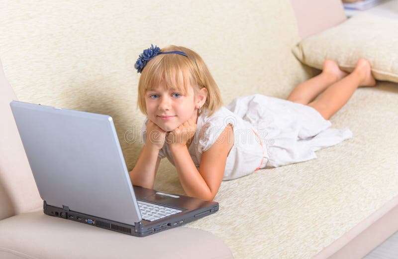 Kleines Mädchen, das auf die Couch mit Laptop legt