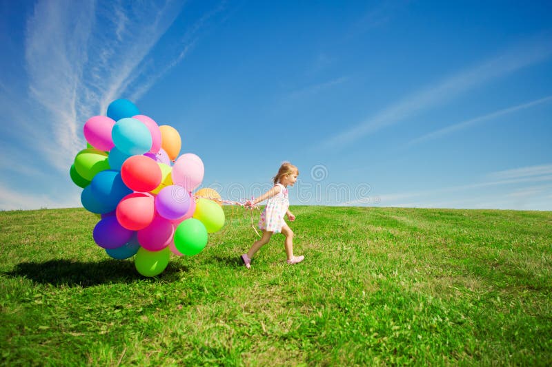 Kleines Mädchen, das bunte Ballone hält. Kind, das auf einem Grün spielt stockfotos