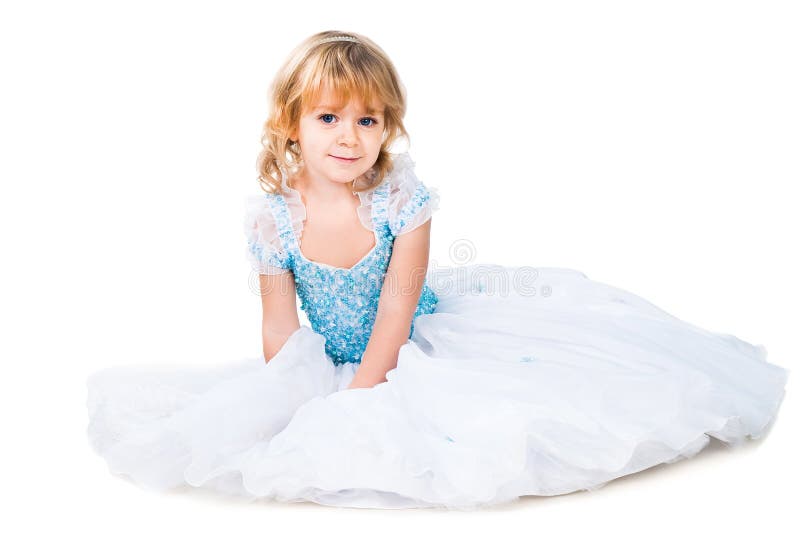 Kleines Mädchen, das im herrlichen blauen Kleid auf Weiß sitzt stockfotografie