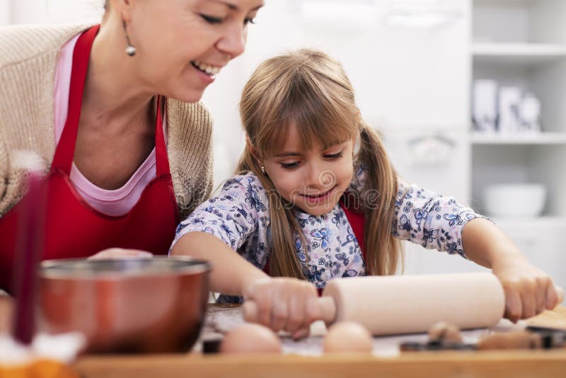 Kleines Mädchen, das mit ihrer Mutter den KeksTeig am Küchentisch ausstreckt lizenzfreie stockfotografie Kleines Mädchen, das mit ihrer Mutter den KeksTeig am Küchentisch ausstreckt lizenzfreie stockfotografie