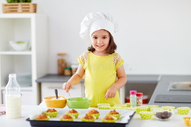 Kleines Mädchen in den Chefs Toque-Backenmuffins zu Hause stockfotografie Kleines Mädchen in den Chefs Toque-Backenmuffins zu Hause stockfotografie