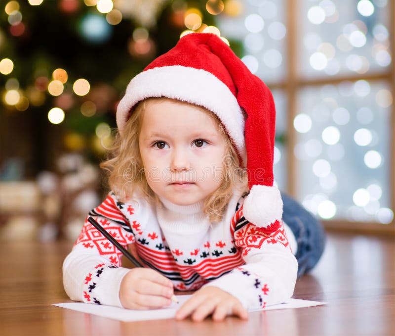 Kleines Mädchen in einem roten Weihnachtshut einen Brief schreibend Santa Cla stockfotografie Kleines Mädchen in einem roten Weihnachtshut einen Brief schreibend Santa Cla stockfotografie