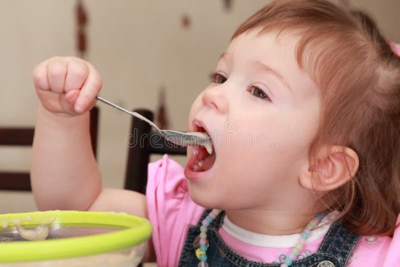 Kleines Mädchen im rosafarbenen Hemd Brei essend lizenzfreies stockfoto