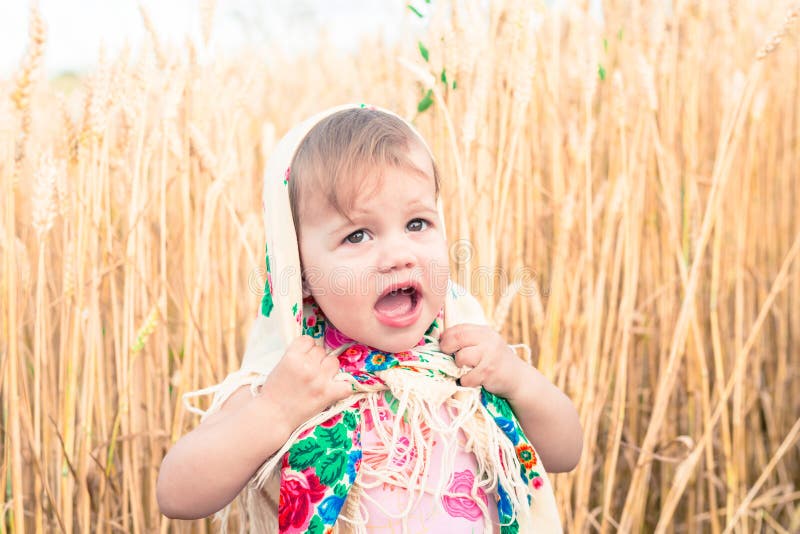 Little girl in national scarf stands in the middle of the field and cries. Orphans, social problems. Little girl in national scarf stands in the middle of the field and cries. Orphans, social problems.