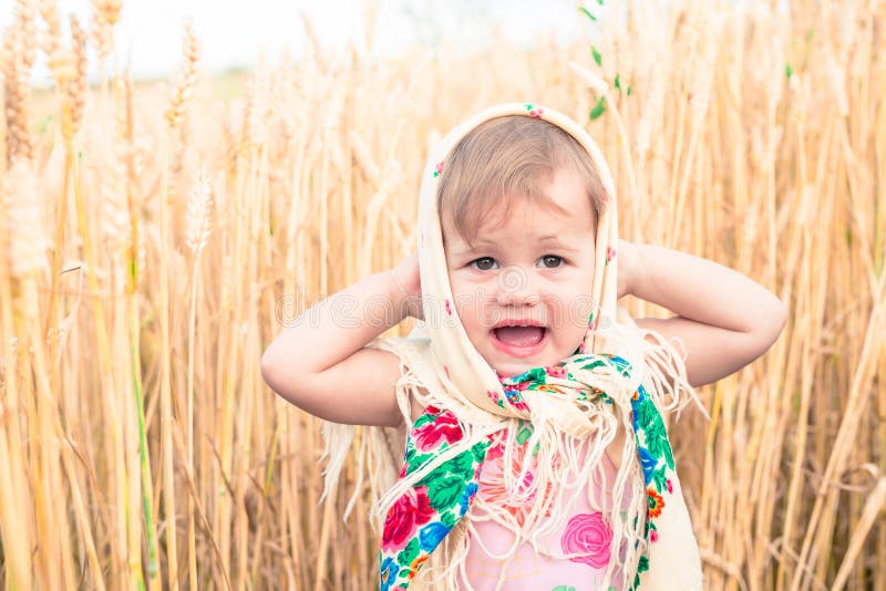 Little girl in national scarf stands in the middle of the field and cries. Orphans, social problems. Little girl in national scarf stands in the middle of the field and cries. Orphans, social problems.