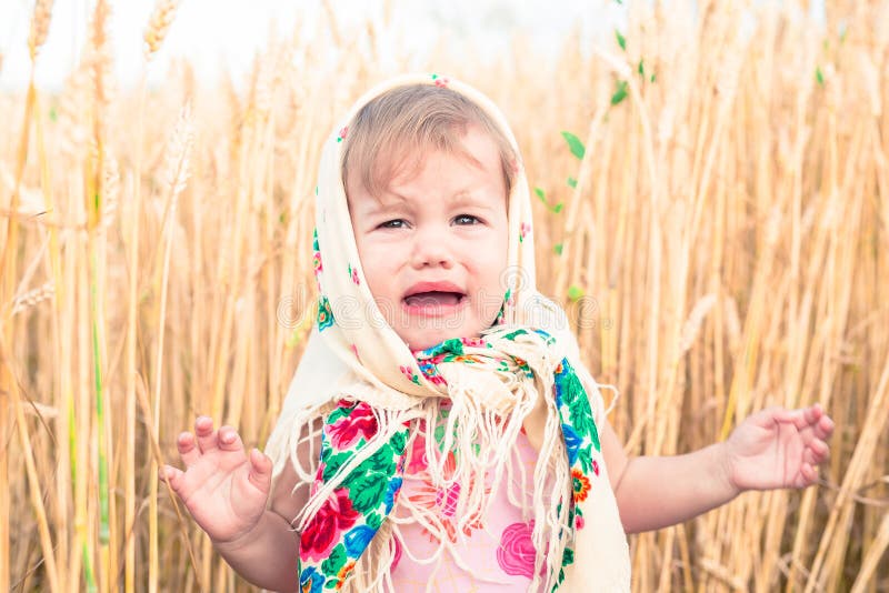 Little girl in national scarf stands in the middle of the field and cries. Orphans, social problems. Little girl in national scarf stands in the middle of the field and cries. Orphans, social problems.