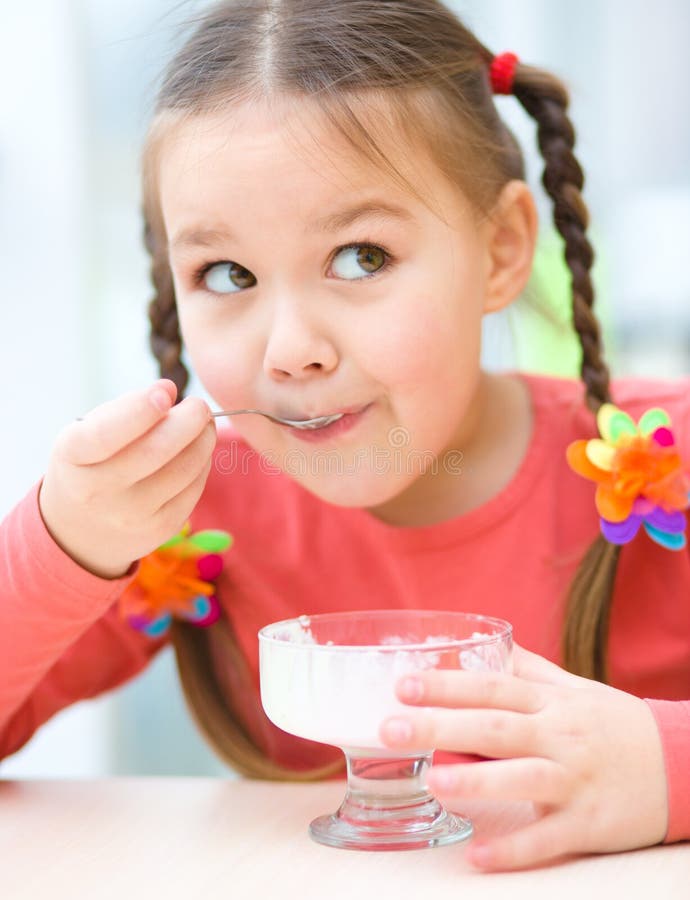 Kleines Mädchen isst Eiscreme im Wohnzimmer lizenzfreie stockfotografie Kleines Mädchen isst Eiscreme im Wohnzimmer lizenzfreie stockfotografie