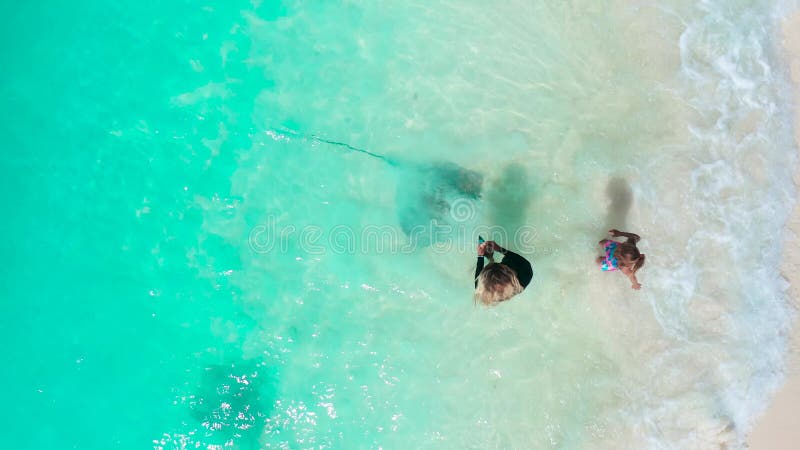 Kleines Mädchen mit Mutter, die Rochen im Wasser am weißen Sandstrand der Insel Fulidhoo füttert. Oberansicht. stock video footage