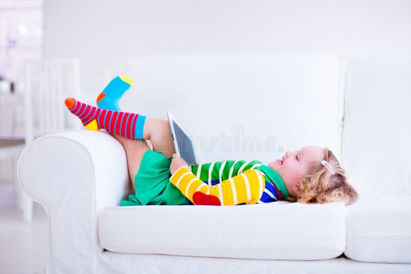 Kleines Mädchen mit Tablet-Computer auf einer weißen Couch lizenzfreie stockfotos Kleines Mädchen mit Tablet-Computer auf einer weißen Couch lizenzfreie stockfotos