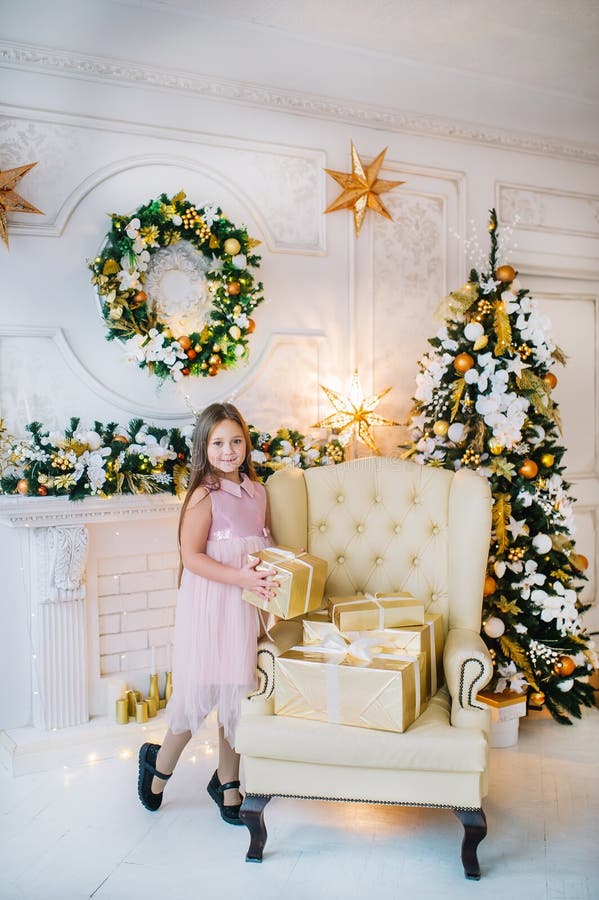 Kleines Mädchen in rosa Kleid steht auf dem Sessel am Weihnachtsbaum im Neujahrszimmer lizenzfreies stockbild Kleines Mädchen in rosa Kleid steht auf dem Sessel am Weihnachtsbaum im Neujahrszimmer lizenzfreies stockbild