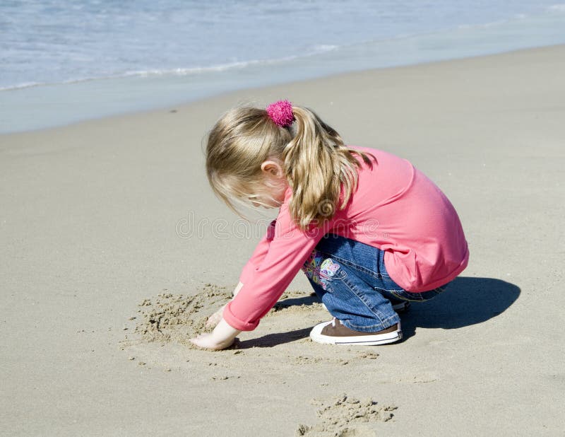 Kleines schönes Mädchen zeichnet auf Sand lizenzfreies stockfoto Kleines schönes Mädchen zeichnet auf Sand lizenzfreies stockfoto