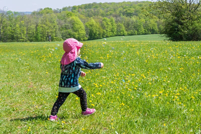 Kleinkind spielt auf sommerlicher Blumenwiese mit Seifenblasen lizenzfreie stockfotografie Kleinkind spielt auf sommerlicher Blumenwiese mit Seifenblasen lizenzfreie stockfotografie