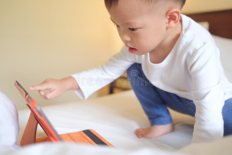 Kleinkindjungenkind, das im Bett spielt mit Tabletten-PC sitzt stockfoto Kleinkindjungenkind, das im Bett spielt mit Tabletten-PC sitzt stockfoto