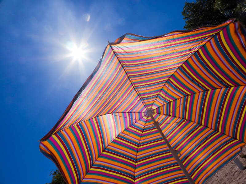 Kleurrijke gestreepte parasol tegen de hemel en de zon Heet weer Een strandvakantie royalty-vrije stock foto Kleurrijke gestreepte parasol tegen de hemel en de zon Heet weer Een strandvakantie royalty-vrije stock foto