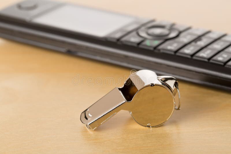 Chrome whistle with telephone on wooden office desk - whistleblower concept, selective focus. Chrome whistle with telephone on wooden office desk - whistleblower concept, selective focus