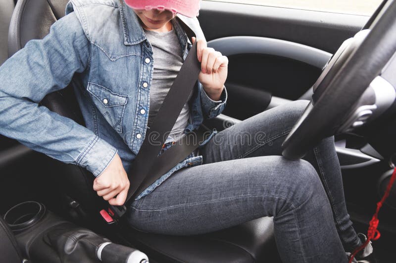 Kläder för jeans för en hipsterflicka fäster bärande hennes säkerhetsbälte i bilen royaltyfria bilder Kläder för jeans för en hipsterflicka fäster bärande hennes säkerhetsbälte i bilen royaltyfria bilder