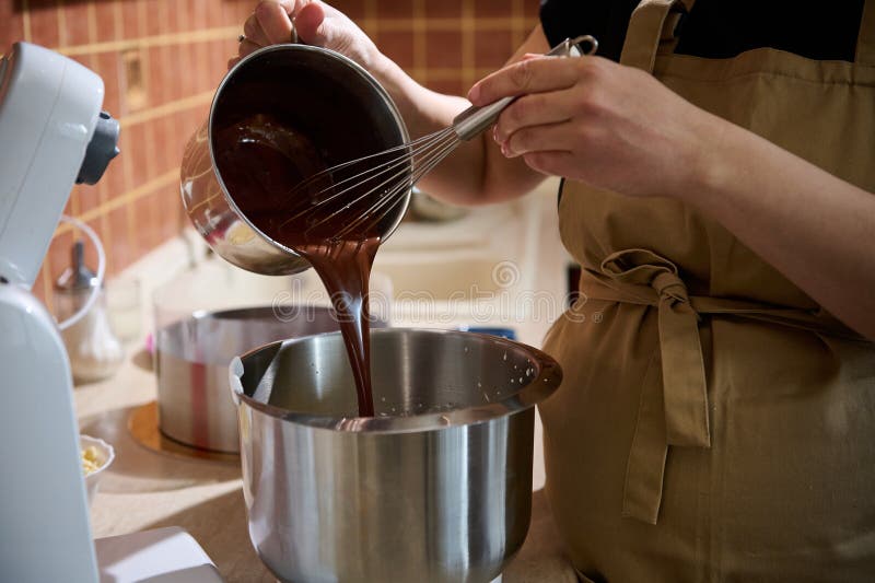 Kläder som häller smält choklad i en planetskål som blandar den med grädde eller vita äggvita arkivbilder