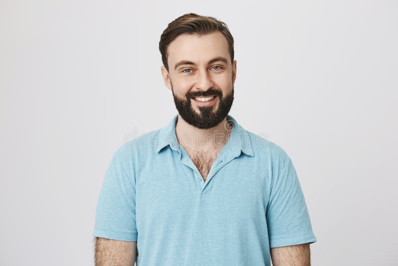 Knappe gebaarde mens in blauwe t-shirt op een witte achtergrond De barman nodigt bezoekers met een brede glimlach op zijn gezicht royalty-vrije stock fotografie Knappe gebaarde mens in blauwe t-shirt op een witte achtergrond De barman nodigt bezoekers met een brede glimlach op zijn gezicht royalty-vrije stock fotografie