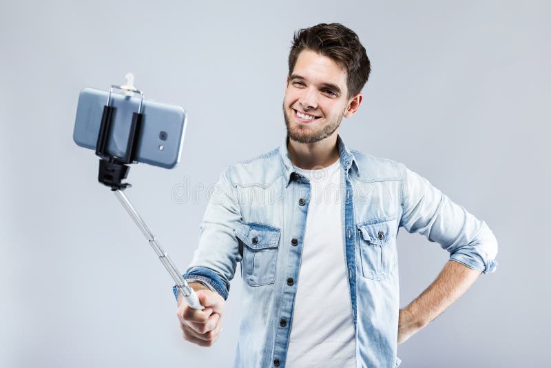 Knappe jonge mens die een selfie over grijze achtergrond nemen stock afbeelding Knappe jonge mens die een selfie over grijze achtergrond nemen stock afbeelding