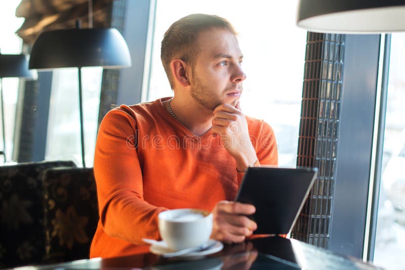 Knappe jonge mens die met tablet, het denken werken, die uit het venster, terwijl het genieten van van koffie in koffie kijken stock fotografie Knappe jonge mens die met tablet, het denken werken, die uit het venster, terwijl het genieten van van koffie in koffie kijken stock fotografie