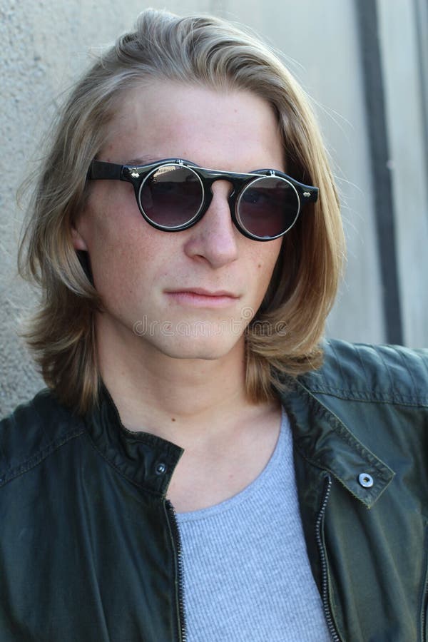 Knappe jonge mens met blond lang die haar en zonnebril op grijze achtergrond wordt geïsoleerd De studioschot van de manier royalty-vrije stock afbeelding Knappe jonge mens met blond lang die haar en zonnebril op grijze achtergrond wordt geïsoleerd De studioschot van de manier royalty-vrije stock afbeelding