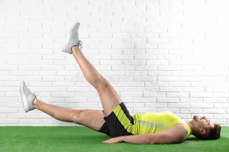 Knappe jonge mens in sportkleding die schaaroefening op kunstmatig groen gazon doen stock fotografie Knappe jonge mens in sportkleding die schaaroefening op kunstmatig groen gazon doen stock fotografie