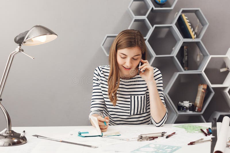 Knappe jonge ondernemersontwerper met donker haar in gestreept overhemd die op telefoon met klant het bespreken spreken
