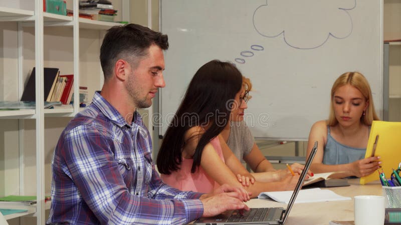 Knappe mannelijke student die duimen tonen terwijl het gebruiken van laptop