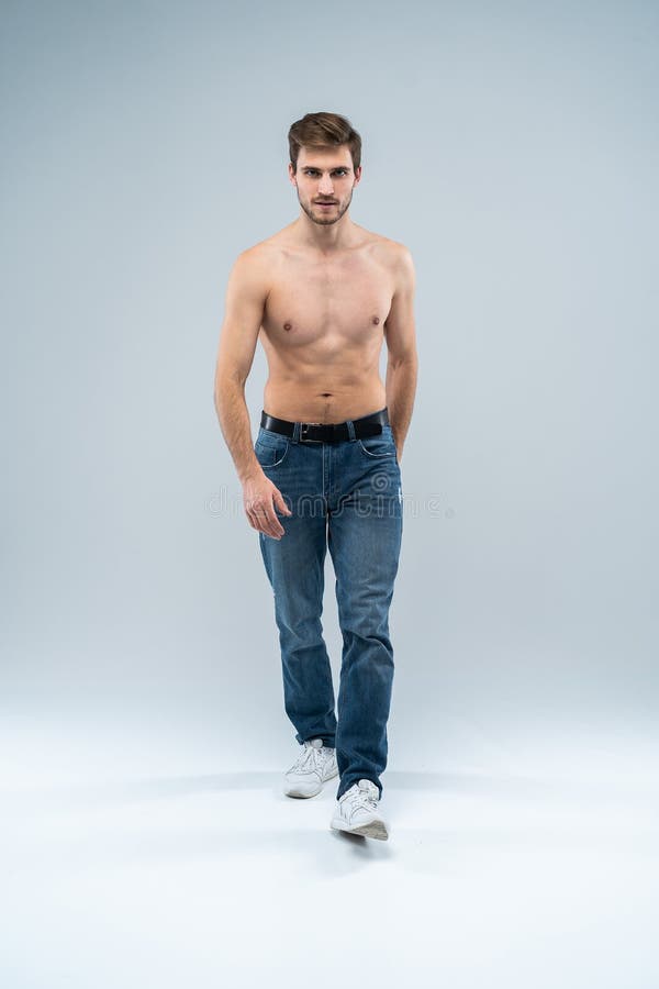 Knappe vrolijke mens Volledige lengte van de knappe jonge shirtless mens die in jeans camera met glimlach bekijkt terwijl status stock afbeelding Knappe vrolijke mens Volledige lengte van de knappe jonge shirtless mens die in jeans camera met glimlach bekijkt terwijl status stock afbeelding