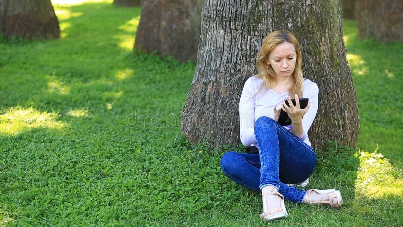 Knappe vrouwenzitting onder een palm en het doorbladeren van Internet op een smartphone