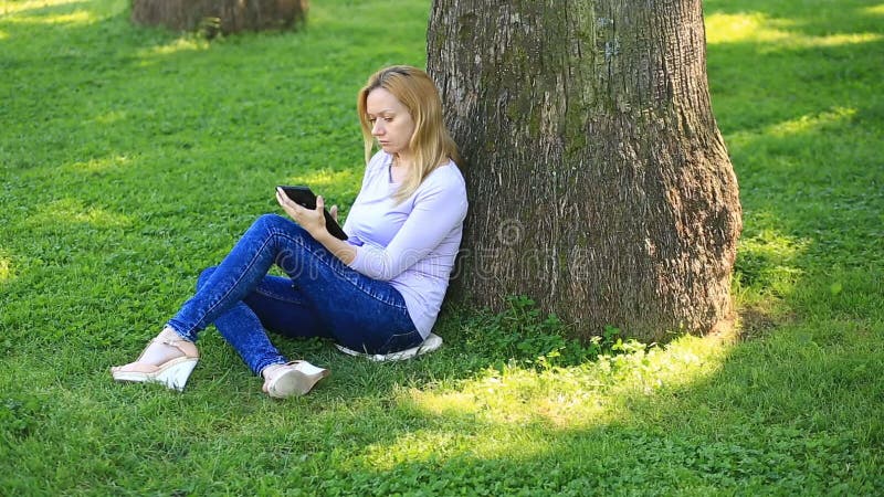 Knappe vrouwenzitting onder een palm en het doorbladeren van Internet op een smartphone