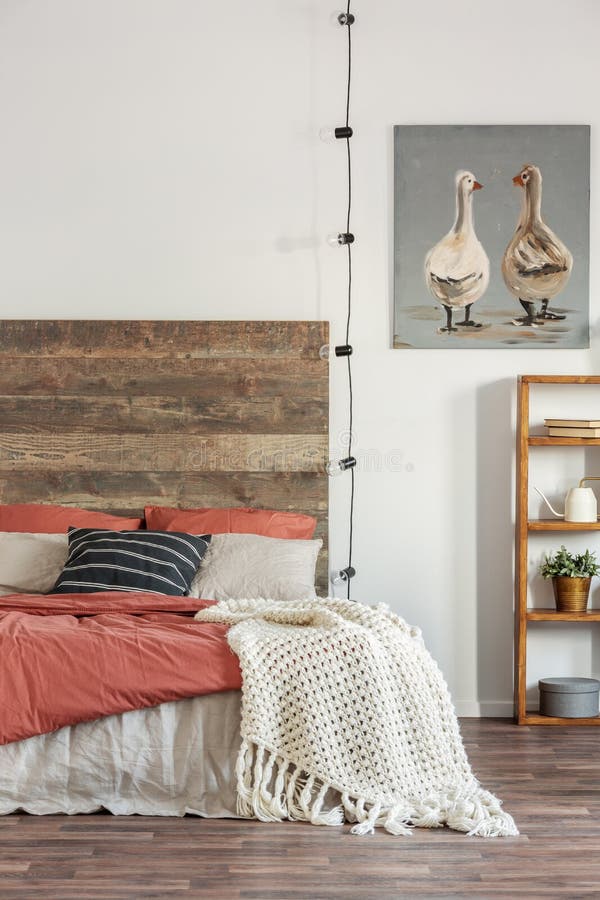 Knit blanket on a bed with wooden bedhead standing against white wall with an oil painting of ducks. Real photo of bedroom