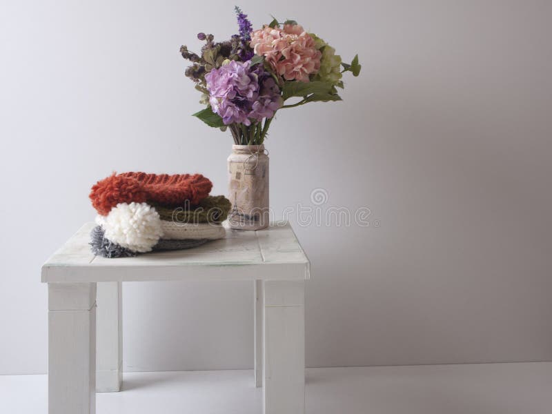 Mano tejer sombreros de varios colores senales, sobre el blanco en mal estado elegante mesa una botella lleno de vistoso Salvaje flores.