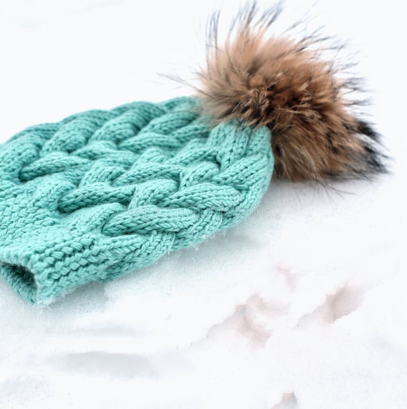 knitted turquoise hat or beanie with pom pom on a snow. winter apparel concept. kids warm clothes and accessories