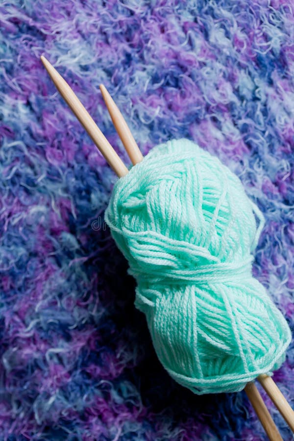 Ball of wool with knitting needles against purple knitted fabric. Ball of wool with knitting needles against purple knitted fabric