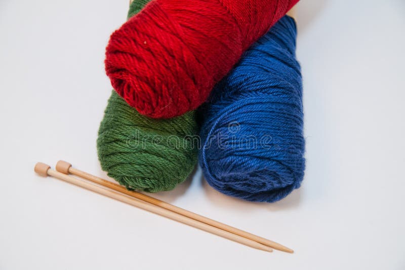 Three primary colored yarn skeins with bamboo knitting needles on a white background with a view from above. Three primary colored yarn skeins with bamboo knitting needles on a white background with a view from above.