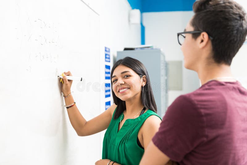 She Knows How To Find The Answers. Smiling pupil writing equation on whiteboard during lecture