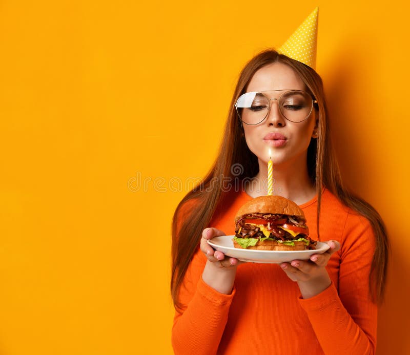 Kobiet ręk chwyta hamburgeru grilla duża kanapka z wołowiną i zaświecającą świeczką dla przyjęcia urodzinowego na kolorze żółtym zdjęcia royalty free Kobiet ręk chwyta hamburgeru grilla duża kanapka z wołowiną i zaświecającą świeczką dla przyjęcia urodzinowego na kolorze żółtym zdjęcia royalty free