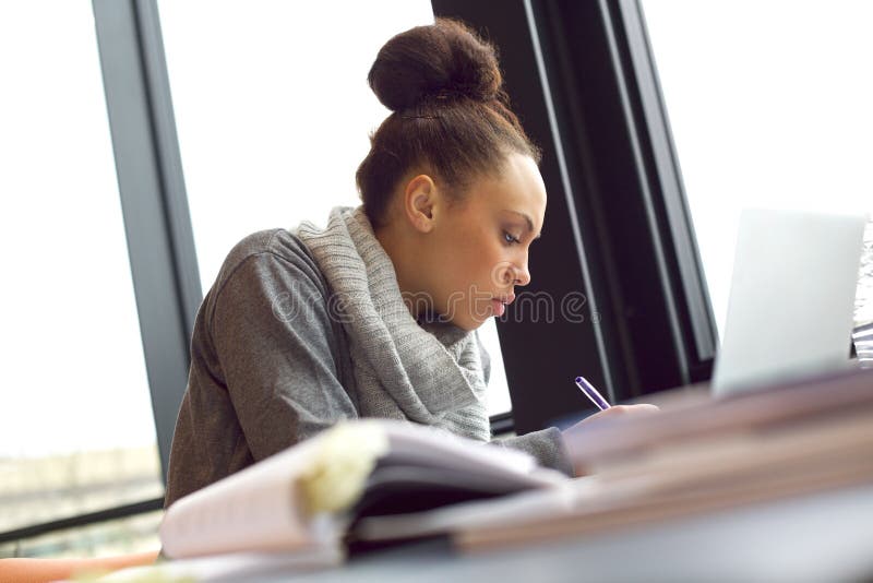 Young african american woman taking notes from books for her study. Sitting at table with books and laptop for finding information. Young african american woman taking notes from books for her study. Sitting at table with books and laptop for finding information.