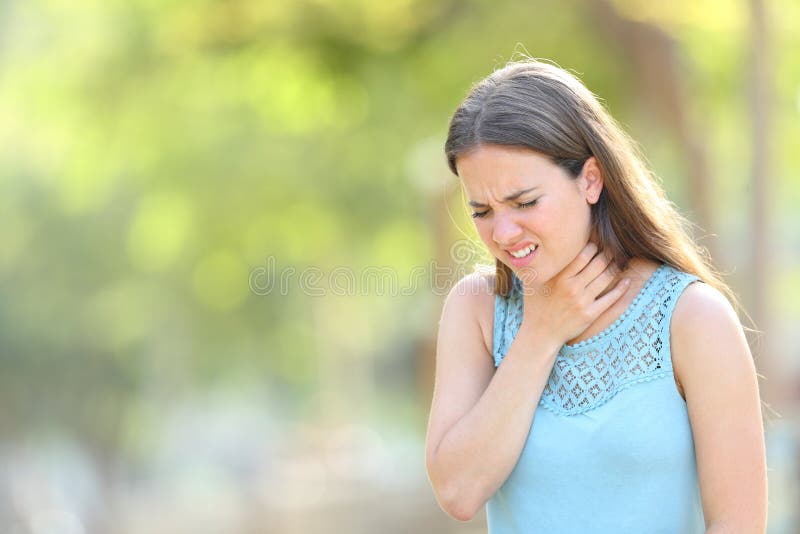 Woman suffering sore throat in a park standing outdoors in a park. Woman suffering sore throat in a park standing outdoors in a park