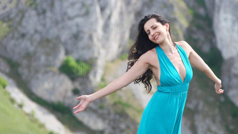 Beautiful young woman on mountain cliff stretching arm and feeling wind and sun. Beautiful young woman on mountain cliff stretching arm and feeling wind and sun