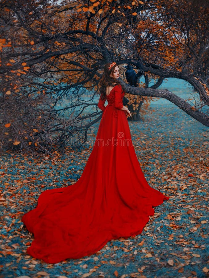 Fantasy woman queen in red dress with long train. Golden crown on head. Autumn nature tree black raven sits on branch, fallen orange leaves on green grass blue fog. rear view back. Girl gothic queen. Fantasy woman queen in red dress with long train. Golden crown on head. Autumn nature tree black raven sits on branch, fallen orange leaves on green grass blue fog. rear view back. Girl gothic queen