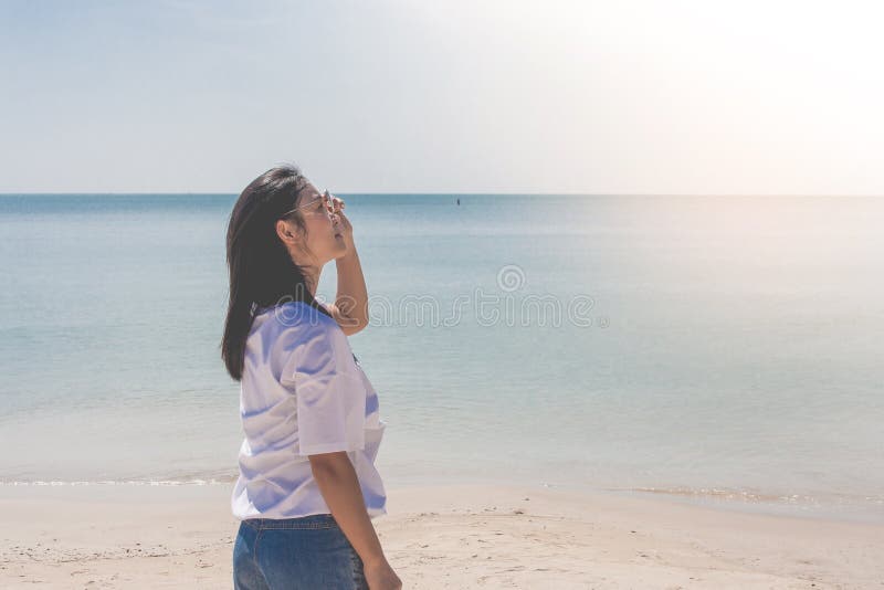 Kobieta jest ubranym białą koszulkę, ona stoi na piasek plaży i trzyma okulary przeciwsłonecznych w ręce z pięknym seascape widok fotografia stock Kobieta jest ubranym białą koszulkę, ona stoi na piasek plaży i trzyma okulary przeciwsłonecznych w ręce z pięknym seascape widok fotografia stock