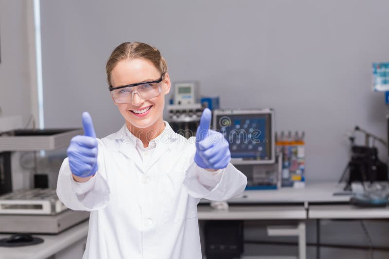 Kobieta-naukowiec stojąca w laboratorium w rękawiczkach płaszczowych i podnosząca kciuki fotografia stock