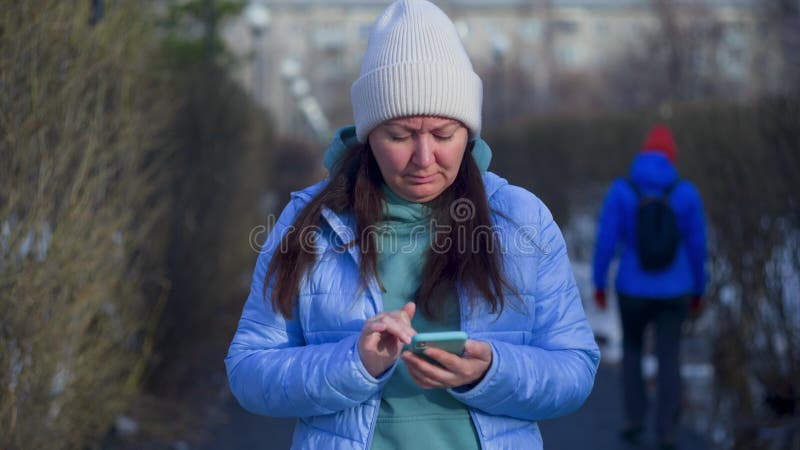 Kobieta oglądająca surfing na smartfonie w Internecie stojąca na ścieżce w parku.