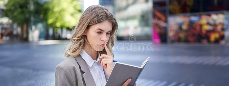 Woman looking concentrated while reading her notes, preparing for interview. Businesswoman in suit writes down in notebook, sits in city centre. Woman looking concentrated while reading her notes, preparing for interview. Businesswoman in suit writes down in notebook, sits in city centre.