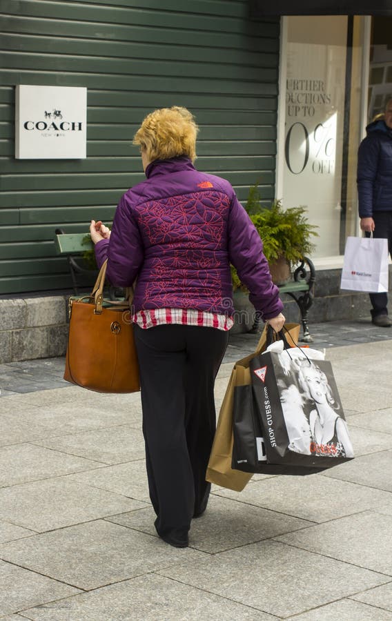 Kobieta pogrążona z przewoźnik torbami podczas gdy cieszący się niektóre detaliczną terapię przy up targowym Kildare wioski zakup fotografia stock Kobieta pogrążona z przewoźnik torbami podczas gdy cieszący się niektóre detaliczną terapię przy up targowym Kildare wioski zakup fotografia stock